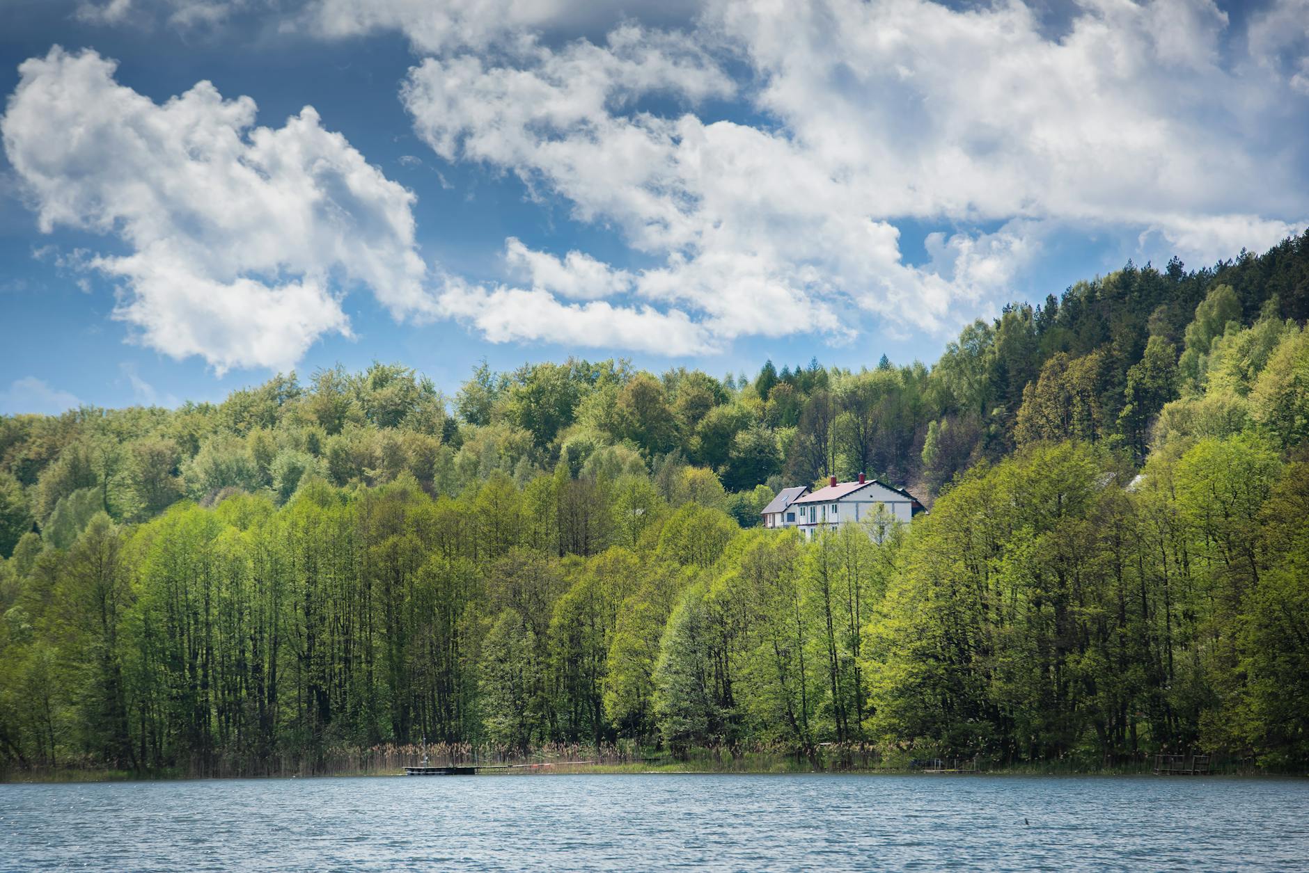 Dom nad jeziorem wśród zielonych drzew w Szymbarku, słoneczna pogoda